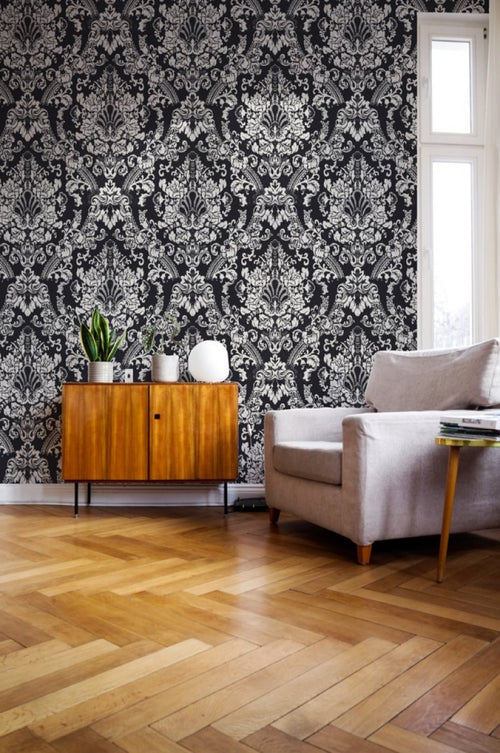 Living room with ornate wallpaper, wooden sideboard, and gray sofa.